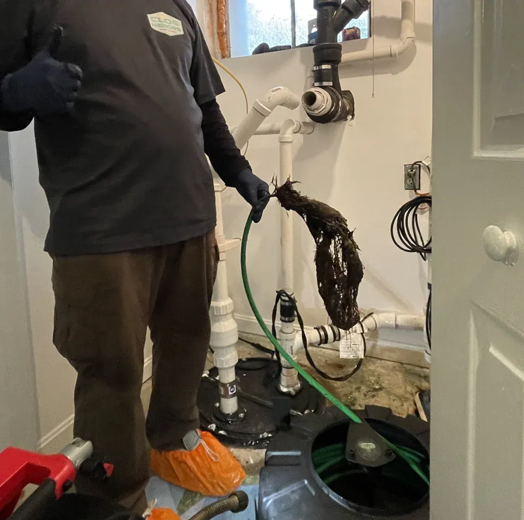 Plumber in shoe covers holding a drain cable with a clump of debris pulled from a basement drain line