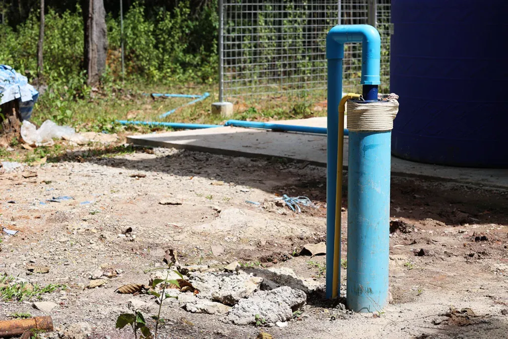 Blue well pipe rising from the ground in a rural yard
