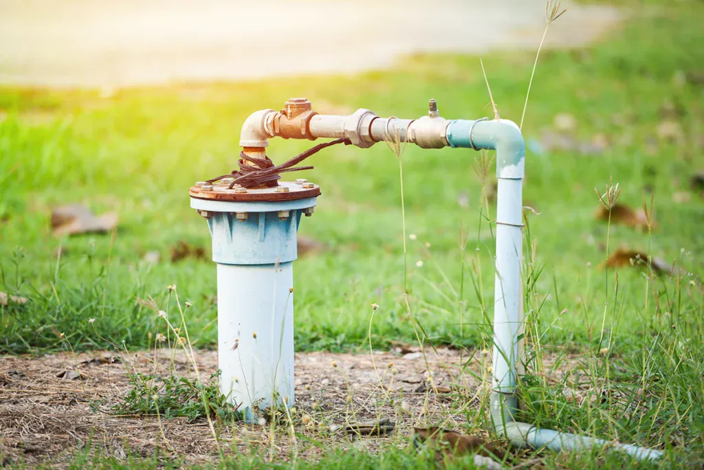 Wellhead cap with a water line running out of it across a grassy yard