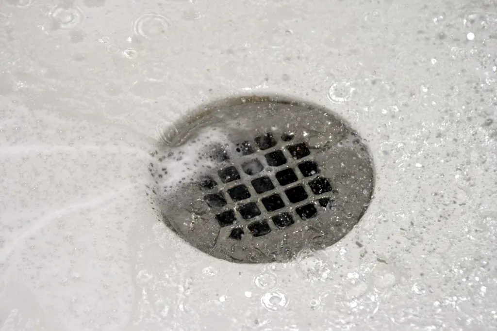 Round stainless shower drain with water and soap suds flowing into it