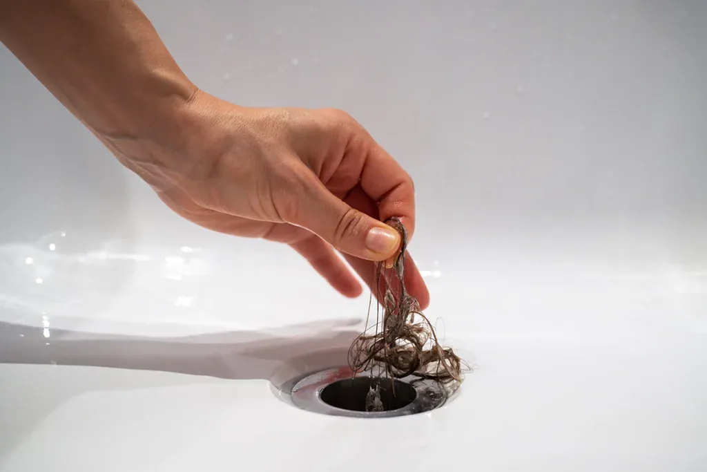 Hand pulling a clump of hair out of a white tub drain