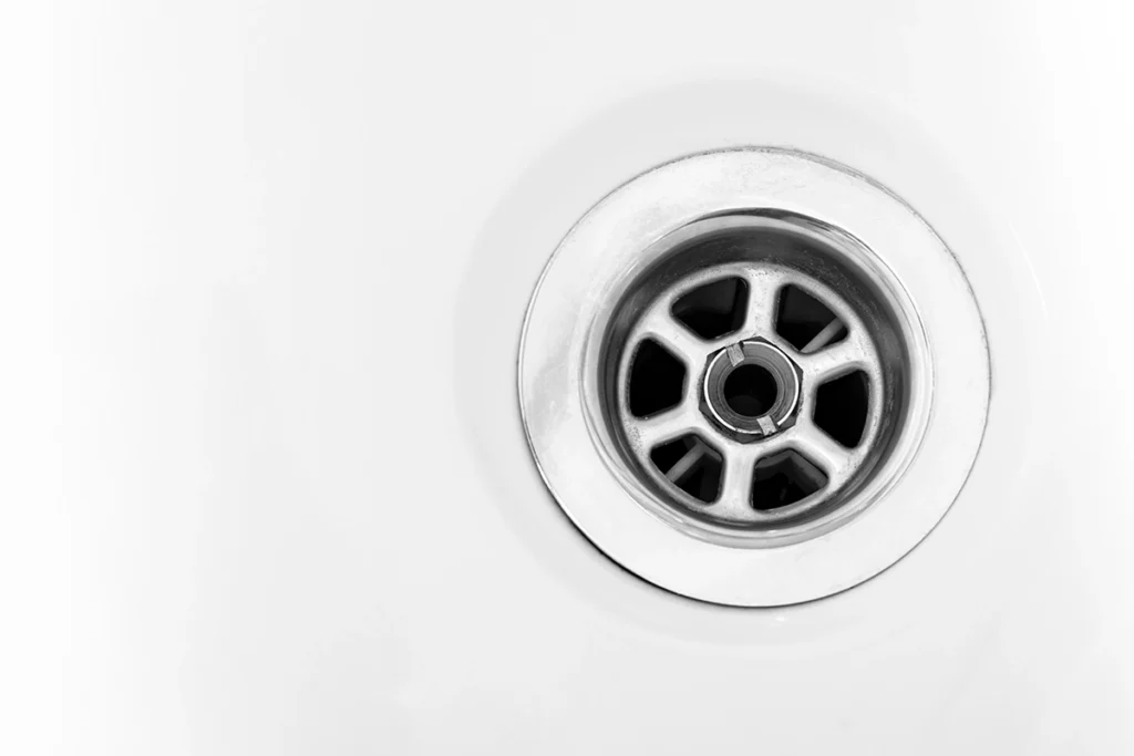 Close-up of a chrome sink drain strainer in a white basin