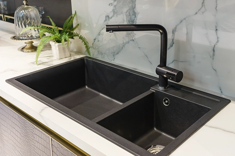 Black double-basin kitchen sink with a matching single-handle faucet set in a white marble counter