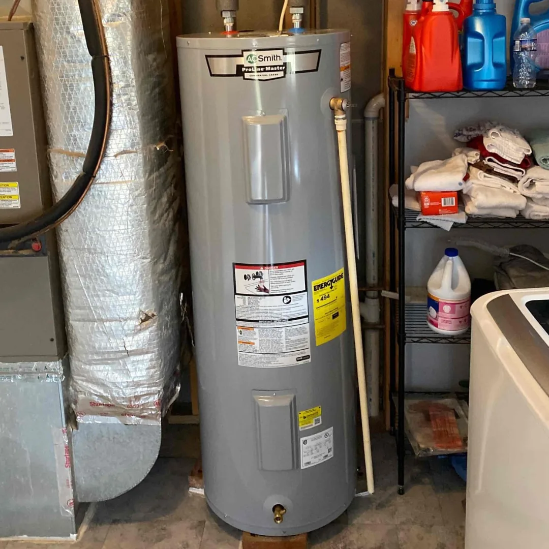 Gray tank water heater standing in a basement utility room beside the furnace ductwork