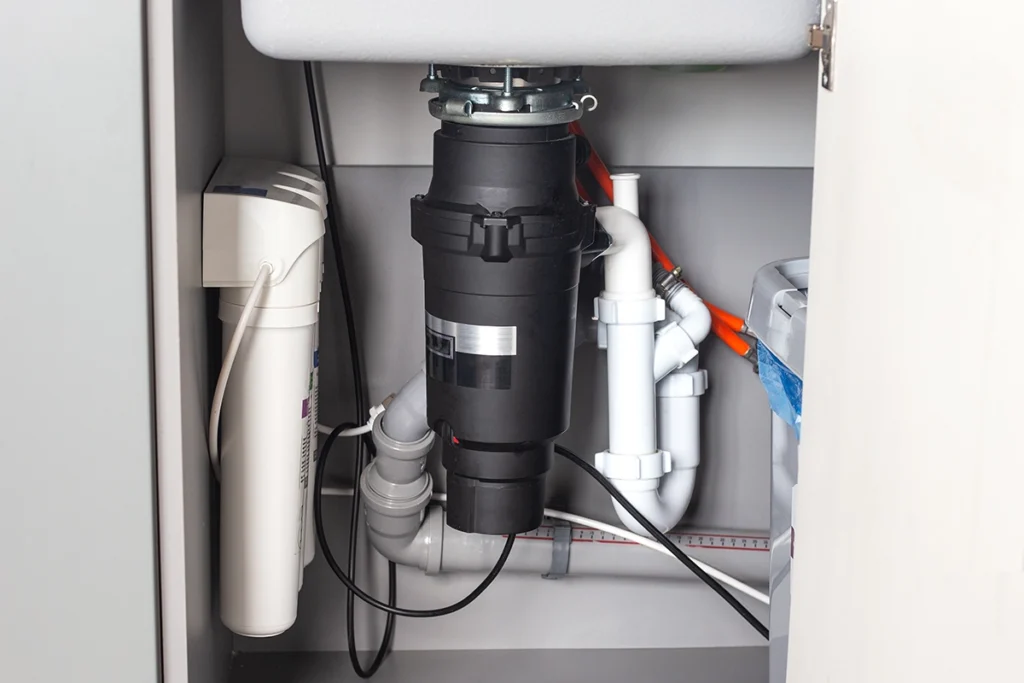 Under-sink cabinet with a garbage disposal, white P-trap drain fittings and a water filter