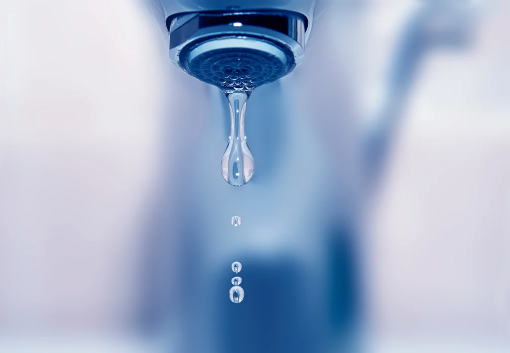 Close-up of a chrome faucet with a drop of water falling from the aerator