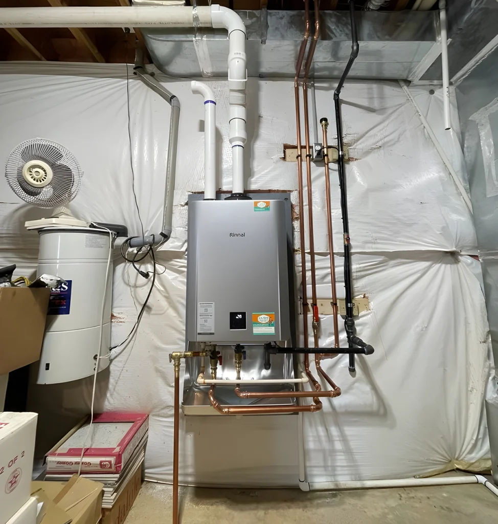 Wall-mounted tankless water heater in an unfinished basement with copper water lines and white PVC venting