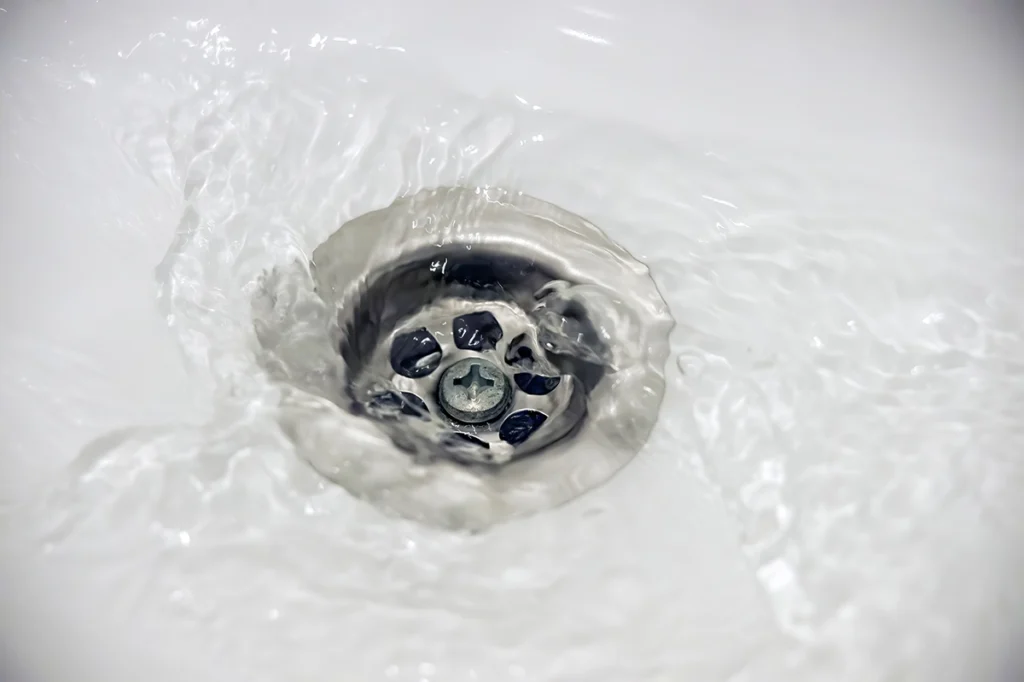 Water swirling down a bathtub drain around a chrome stopper
