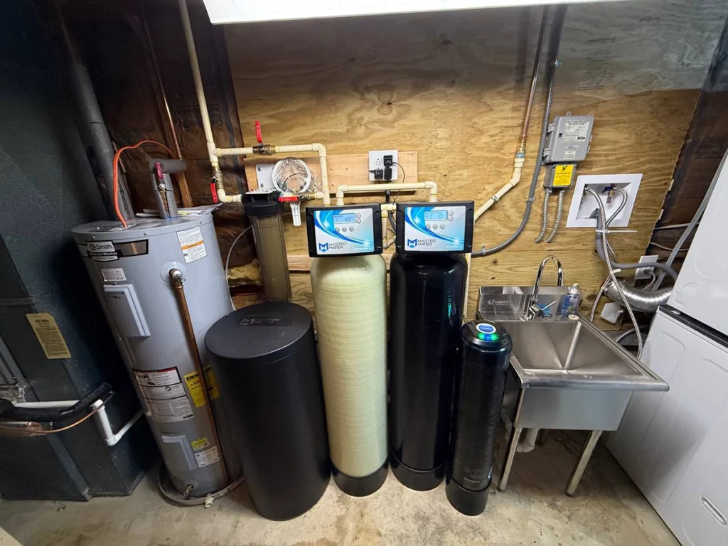Water softener and filter tanks with a brine tank installed beside an electric water heater in a utility room