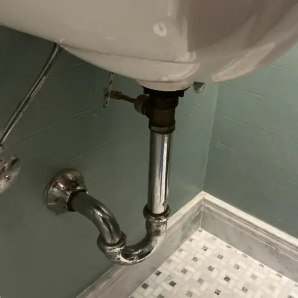 Before: Aging chrome P-trap under a wall-hung bathroom sink.