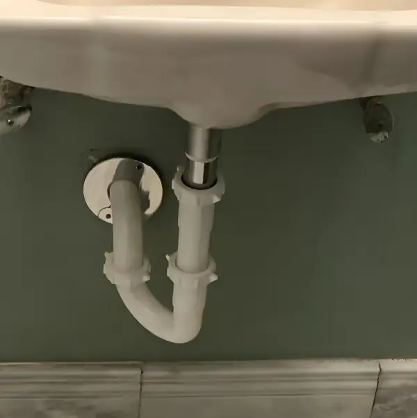 After: New white PVC P-trap installed under the wall-hung bathroom sink.
