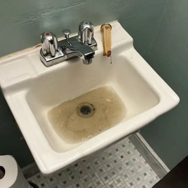 Before: Bathroom sink basin holding brown standing water from a clogged drain.