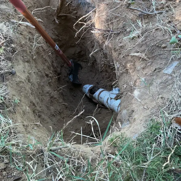 Before: Damaged sewer line exposed at the bottom of a hand-dug excavation.