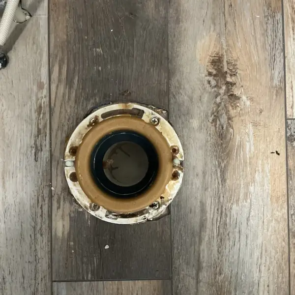 Before: Old toilet flange with wax ring residue on a wood-look floor.