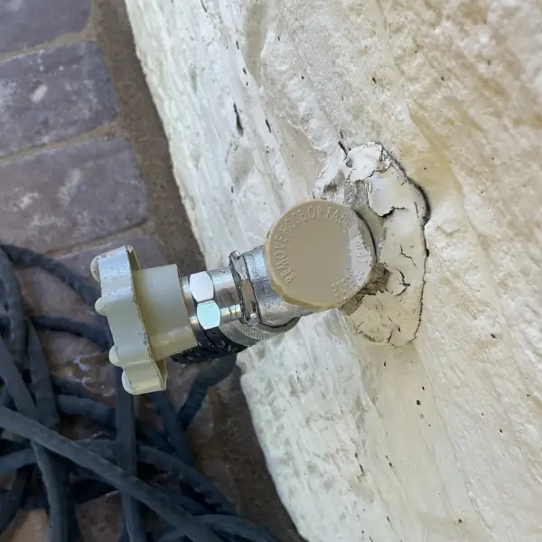 Before: Old leaking hose bib on a painted brick wall.